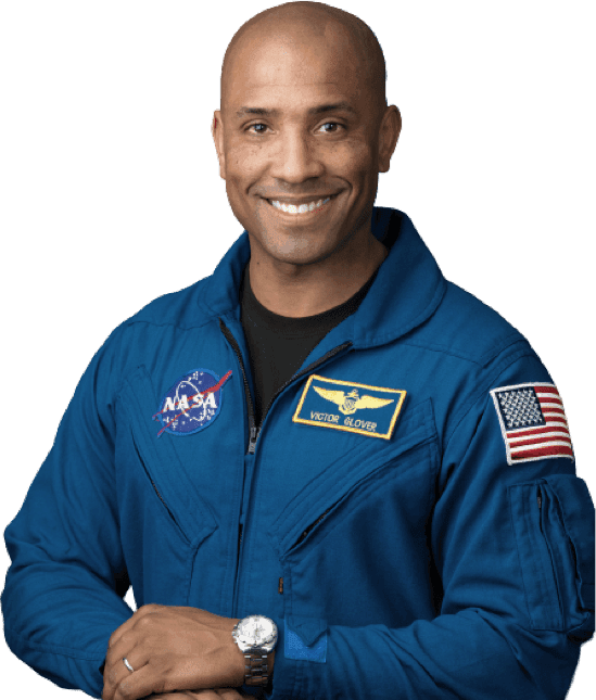 Victor Glover: A man with a shaved head, wearing a NASA blue flight suit and smiling